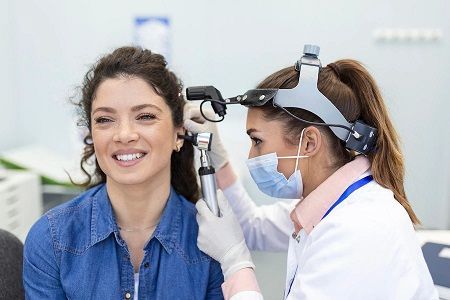A friendly doctor examines a woman's ears during a check-up in a clinical setting.